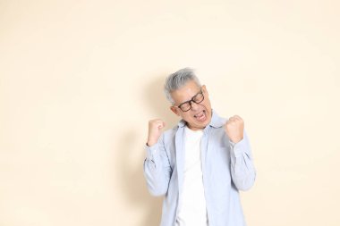 Doğu Asyalı bir adamın portresi gri saçlı ve gözlüklü, şık günlük kıyafetler giymiş, kahverengi arka planda duruyor..