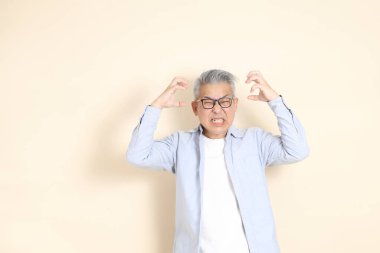 Doğu Asyalı bir adamın portresi gri saçlı ve gözlüklü, şık günlük kıyafetler giymiş, kahverengi arka planda duruyor..