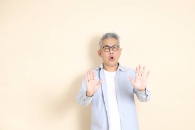 Doğu Asyalı bir adamın portresi gri saçlı ve gözlüklü, şık günlük kıyafetler giymiş, kahverengi arka planda duruyor..