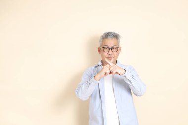 Doğu Asyalı bir adamın portresi gri saçlı ve gözlüklü, şık günlük kıyafetler giymiş, kahverengi arka planda duruyor..