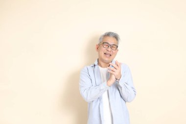 Doğu Asyalı bir adamın portresi gri saçlı ve gözlüklü, şık günlük kıyafetler giymiş, kahverengi arka planda duruyor..