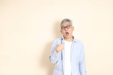 Doğu Asyalı bir adamın portresi gri saçlı ve gözlüklü, şık günlük kıyafetler giymiş, kahverengi arka planda duruyor..