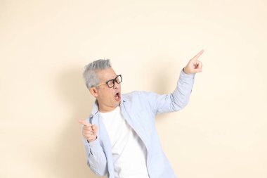 Doğu Asyalı bir adamın portresi gri saçlı ve gözlüklü, şık günlük kıyafetler giymiş, kahverengi arka planda duruyor..