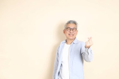 Doğu Asyalı bir adamın portresi gri saçlı ve gözlüklü, şık günlük kıyafetler giymiş, kahverengi arka planda duruyor..