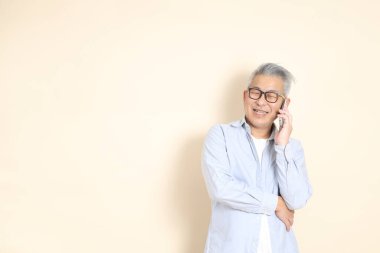 Doğu Asyalı bir adamın portresi gri saçlı ve gözlüklü, şık günlük kıyafetler giymiş, kahverengi arka planda duruyor..