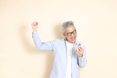 Doğu Asyalı bir adamın portresi gri saçlı ve gözlüklü, şık günlük kıyafetler giymiş, kahverengi arka planda duruyor..