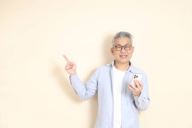 Doğu Asyalı bir adamın portresi gri saçlı ve gözlüklü, şık günlük kıyafetler giymiş, kahverengi arka planda duruyor..