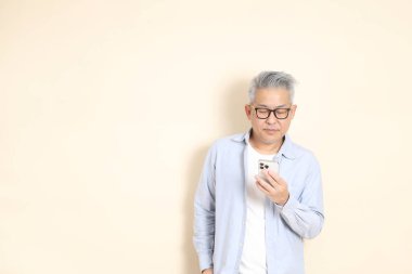 Doğu Asyalı bir adamın portresi gri saçlı ve gözlüklü, şık günlük kıyafetler giymiş, kahverengi arka planda duruyor..