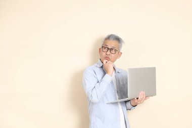 Doğu Asyalı bir adamın portresi gri saçlı ve gözlüklü, şık günlük kıyafetler giymiş, kahverengi arka planda duruyor..