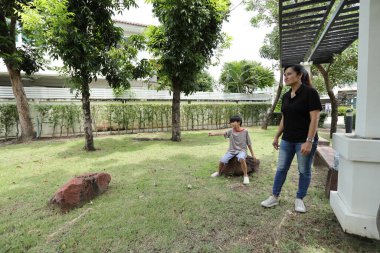 Güneydoğu Asya 'lı bekar bir anne çocuğuyla parkta vakit geçirir ve bitki, böcek ve doğal çevre gibi doğa temelli öğrenme faaliyetleriyle ilgilenir..