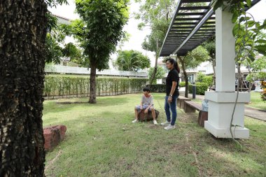 Güneydoğu Asya 'lı bekar bir anne çocuğuyla parkta vakit geçirir ve bitki, böcek ve doğal çevre gibi doğa temelli öğrenme faaliyetleriyle ilgilenir..