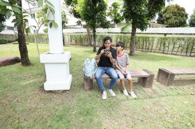 Güneydoğu Asya 'lı bekar bir anne çocuğuyla parkta vakit geçirir ve bitki, böcek ve doğal çevre gibi doğa temelli öğrenme faaliyetleriyle ilgilenir..