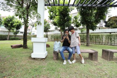 Güneydoğu Asya 'lı bekar bir anne çocuğuyla parkta vakit geçirir ve bitki, böcek ve doğal çevre gibi doğa temelli öğrenme faaliyetleriyle ilgilenir..