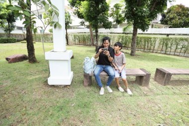 Güneydoğu Asya 'lı bekar bir anne çocuğuyla parkta vakit geçirir ve bitki, böcek ve doğal çevre gibi doğa temelli öğrenme faaliyetleriyle ilgilenir..