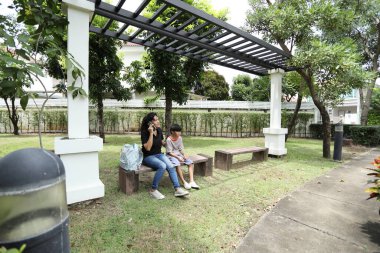 Güneydoğu Asya 'lı bekar bir anne çocuğuyla parkta vakit geçirir ve bitki, böcek ve doğal çevre gibi doğa temelli öğrenme faaliyetleriyle ilgilenir..