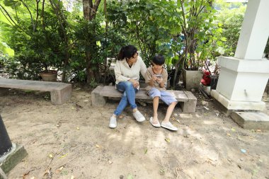 Güneydoğu Asya 'lı bekar bir anne çocuğuyla parkta vakit geçirir ve bitki, böcek ve doğal çevre gibi doğa temelli öğrenme faaliyetleriyle ilgilenir..