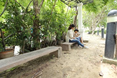 Güneydoğu Asya 'lı bekar bir anne çocuğuyla parkta vakit geçirir ve bitki, böcek ve doğal çevre gibi doğa temelli öğrenme faaliyetleriyle ilgilenir..