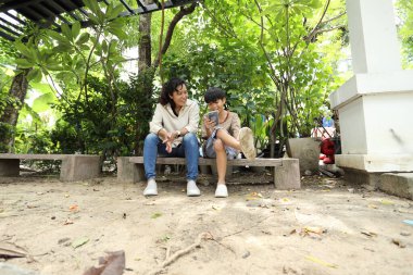 Güneydoğu Asya 'lı bekar bir anne çocuğuyla parkta vakit geçirir ve bitki, böcek ve doğal çevre gibi doğa temelli öğrenme faaliyetleriyle ilgilenir..