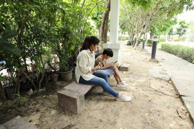 Güneydoğu Asya 'lı bekar bir anne çocuğuyla parkta vakit geçirir ve bitki, böcek ve doğal çevre gibi doğa temelli öğrenme faaliyetleriyle ilgilenir..