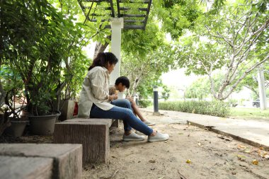Güneydoğu Asya 'lı bekar bir anne çocuğuyla parkta vakit geçirir ve bitki, böcek ve doğal çevre gibi doğa temelli öğrenme faaliyetleriyle ilgilenir..