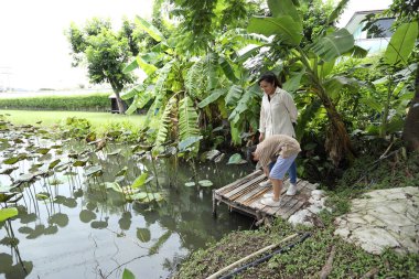 Güneydoğu Asya 'lı bekar bir anne çocuğuyla parkta vakit geçirir ve bitki, böcek ve doğal çevre gibi doğa temelli öğrenme faaliyetleriyle ilgilenir..