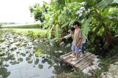 Güneydoğu Asya 'lı bekar bir anne çocuğuyla parkta vakit geçirir ve bitki, böcek ve doğal çevre gibi doğa temelli öğrenme faaliyetleriyle ilgilenir..