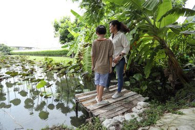 Güneydoğu Asya 'lı bekar bir anne çocuğuyla parkta vakit geçirir ve bitki, böcek ve doğal çevre gibi doğa temelli öğrenme faaliyetleriyle ilgilenir..