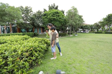 Güneydoğu Asya 'lı bekar bir anne çocuğuyla parkta vakit geçirir ve bitki, böcek ve doğal çevre gibi doğa temelli öğrenme faaliyetleriyle ilgilenir..