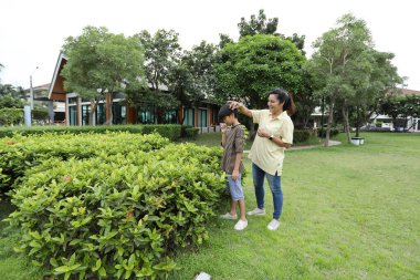 Güneydoğu Asya 'lı bekar bir anne çocuğuyla parkta vakit geçirir ve bitki, böcek ve doğal çevre gibi doğa temelli öğrenme faaliyetleriyle ilgilenir..