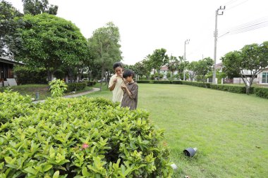 Güneydoğu Asya 'lı bekar bir anne çocuğuyla parkta vakit geçirir ve bitki, böcek ve doğal çevre gibi doğa temelli öğrenme faaliyetleriyle ilgilenir..