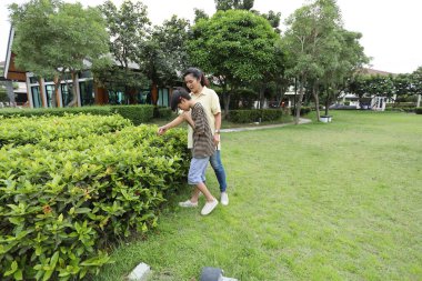 Güneydoğu Asya 'lı bekar bir anne çocuğuyla parkta vakit geçirir ve bitki, böcek ve doğal çevre gibi doğa temelli öğrenme faaliyetleriyle ilgilenir..