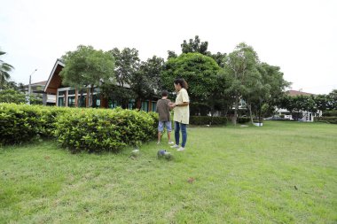 Güneydoğu Asya 'lı bekar bir anne çocuğuyla parkta vakit geçirir ve bitki, böcek ve doğal çevre gibi doğa temelli öğrenme faaliyetleriyle ilgilenir..