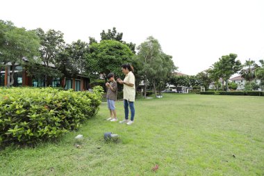 Güneydoğu Asya 'lı bekar bir anne çocuğuyla parkta vakit geçirir ve bitki, böcek ve doğal çevre gibi doğa temelli öğrenme faaliyetleriyle ilgilenir..