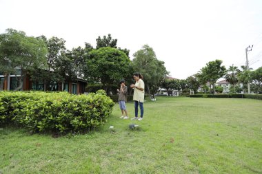 Güneydoğu Asya 'lı bekar bir anne çocuğuyla parkta vakit geçirir ve bitki, böcek ve doğal çevre gibi doğa temelli öğrenme faaliyetleriyle ilgilenir..