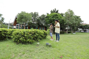 Güneydoğu Asya 'lı bekar bir anne çocuğuyla parkta vakit geçirir ve bitki, böcek ve doğal çevre gibi doğa temelli öğrenme faaliyetleriyle ilgilenir..