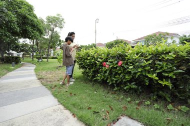Güneydoğu Asya 'lı bekar bir anne çocuğuyla parkta vakit geçirir ve bitki, böcek ve doğal çevre gibi doğa temelli öğrenme faaliyetleriyle ilgilenir..