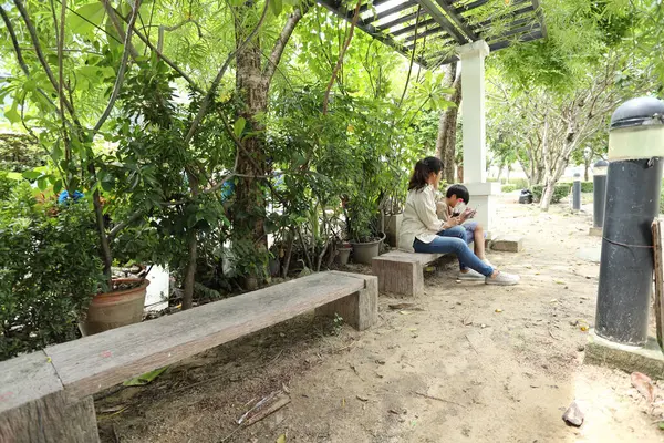 Güneydoğu Asya 'lı bekar bir anne çocuğuyla parkta vakit geçirir ve bitki, böcek ve doğal çevre gibi doğa temelli öğrenme faaliyetleriyle ilgilenir..