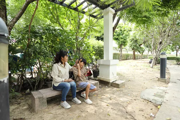 Güneydoğu Asya 'lı bekar bir anne çocuğuyla parkta vakit geçirir ve bitki, böcek ve doğal çevre gibi doğa temelli öğrenme faaliyetleriyle ilgilenir..