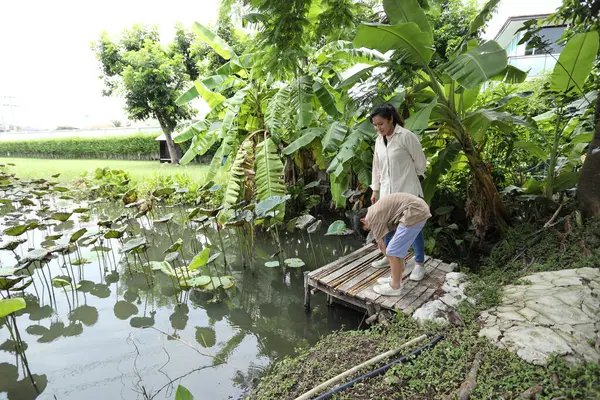 Güneydoğu Asya 'lı bekar bir anne çocuğuyla parkta vakit geçirir ve bitki, böcek ve doğal çevre gibi doğa temelli öğrenme faaliyetleriyle ilgilenir..