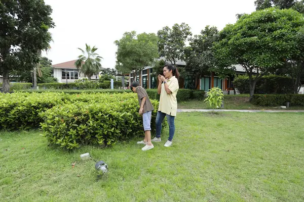 Güneydoğu Asya 'lı bekar bir anne çocuğuyla parkta vakit geçirir ve bitki, böcek ve doğal çevre gibi doğa temelli öğrenme faaliyetleriyle ilgilenir..