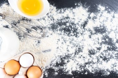 Pişirme malzemeleri kopyalama alanı ile arka plan. Un, yumurta, süt, un kaplı siyah tahta yüzeyde fırın. Üst manzara, düz yatış. Model menüsü, afiş, site başlığı, pişirme kavramı