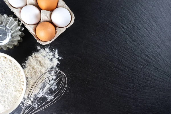 stock image Baking cooking Ingredients background with copy space. Flour, eggs, milk, bakeware on black slate surface. Top view, flat lay. Mockup menu, banner, header for site, baking concept