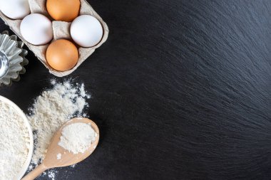 Pişirme malzemeleri kopyalama alanı ile arka plan. Siyah tahta yüzeyde un, yumurta, süt, fırın malzemesi. Üst manzara, düz yatış. Model menüsü, afiş, site başlığı, pişirme kavramı