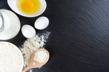 Pişirme malzemeleri kopyalama alanı ile arka plan. Siyah tahta yüzeyde un, yumurta, süt, fırın malzemesi. Üst manzara, düz yatış. Model menüsü, afiş, site başlığı, pişirme kavramı