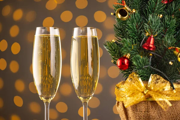 stock image Two wine glasses with bubbly champagne and Christmas tree with decor on background of blurry sparkling lights. Happy New Year holiday greeting card, banner, header with copy space