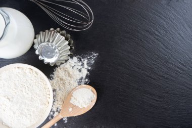 Pişirme malzemeleri kopyalama alanı ile arka plan. Siyah tahta yüzeyde un, yumurta, süt, fırın malzemesi. Üst manzara, düz yatış. Model menüsü, afiş, site başlığı, pişirme kavramı