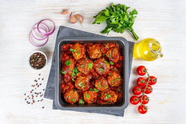 Homemade meatballs with tomato sauce and spices served in black pan on white wooden background. Tasty cooked meat balls made with minced beef and food ingredients. Top View, Flat lay.