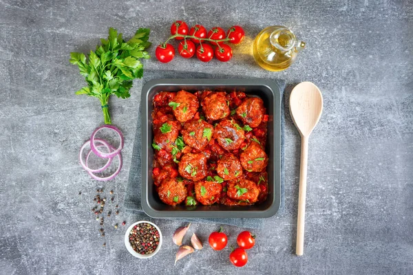 Homemade meatballs with tomato sauce and spices served in black pan on grey concrete background. Tasty cooked meat balls made with minced beef and food ingredients. Top View, Flat lay.