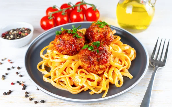 Homemade spaghetti with tomato sauce meatballs and spices served in black plate on white wooden background. Tasty cooked pasta with minced beef meat balls and food ingredients
