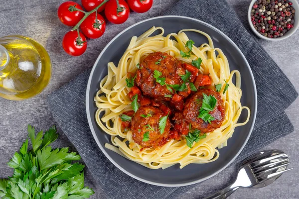 Homemade spaghetti with tomato sauce meatballs and spices served in black plate on gray concrete background. Tasty cooked pasta with minced beef meat balls and food ingredients. Top View, Flat lay.